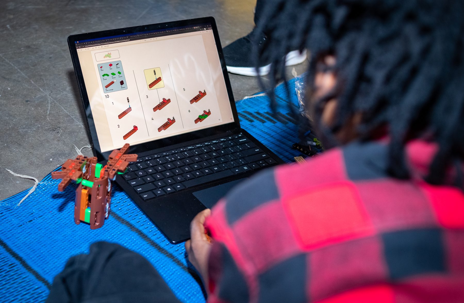 Young innovators assembling a robotics prototype from a build guide on a laptop