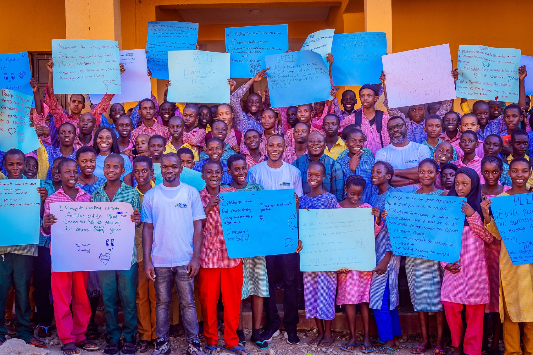 Students and CCAIE facilitators holding blue climate pledge posters